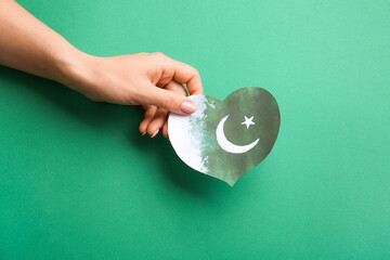 Female hand with flag of Pakistan in shape of heart on color background