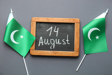 Flags of Pakistan and chalkboard with date of Independence Day on grey background - obrazy, fototapety, plakaty