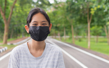Portrait cheerful adorable Thai teen girl wears black face mask standing on the footpath in public park during COVID-19 epidemic. Healthy lifestyle. Pollution free environment. - 447825836