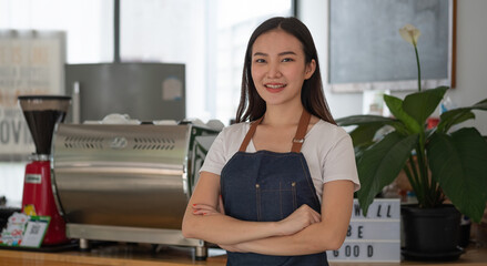 Beautiful asian woman store owner with standing in her coffee shop looking at camera and smiling.Portrait of girl waitress wearing apron and standing in front.