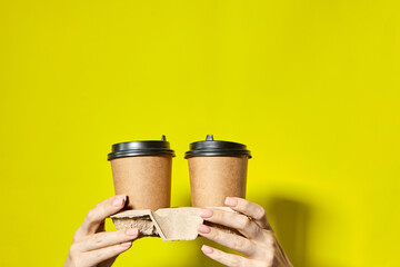 Hands holding two cups brown paper with black lid. Two coffee special offer or promo. Hands holding two cups on yellow screen background. Tea or Coffee to go. Brown paper cup with black lid.