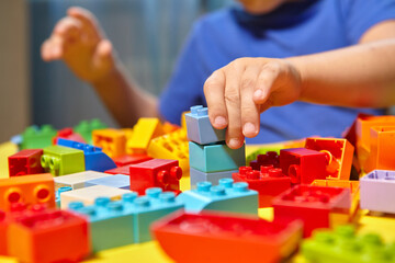 A beautiful boy is playing at home with building blocks. A cute smiling boy is playing with a blocks constructor with a lot of colorful plastic blocks in the room, building a city. Preschool classes.