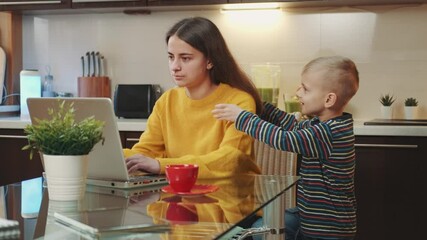 Woman finishing her remote work to spent time with her son. Boy hugging mother and getting on her knees.