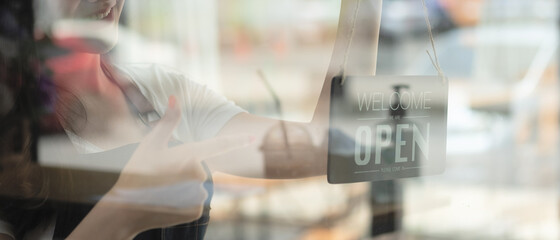 Portrait of smiling young barista girl in apron holding open sign board while standing at her cafe. elegant asian coffee shop female staff turn door plate in the morning in own store small business