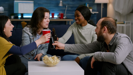 Multi ethnic friends enjoying time spend together relaxing on couch during home party. Group of multi-ethnic people hanging out, socializing during wekeend party late at night in living room