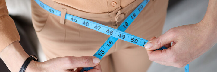 Woman in trousers measuring waist with centimeter tape closeup