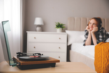Young woman listening to music in bedroom, focus on turntable