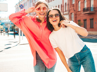 Two young beautiful smiling hipster female in trendy summer white t-shirt clothes and jeans.Sexy carefree women posing on the street background. Positive models having fun, hugging and going crazy