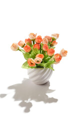 Subject shot of creamy orange tulips in little white ceramic pot. Fine faux flowers for interior design are isolated on the white background. 
