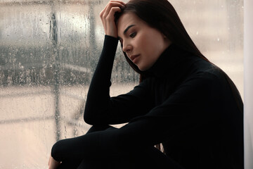 Depressed woman near window on rainy day