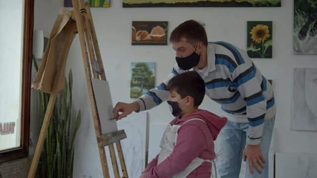 Teacher teaching a boy to draw on a canvas