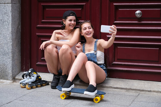 Two women smiling and taking a selfie, holding a skateboard and inline skates.