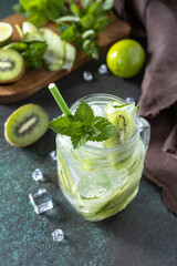 Summer refreshing drink with kiwi, cucumber, lime and ice, mojito or soda with cucumber on a dark stone table. Copy space.