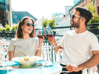 Smiling beautiful woman and her handsome boyfriend. Happy cheerful family. Couple cheering with glasses of red wine at their date in restaurant. They drinking alcohol at veranda cafe in the street