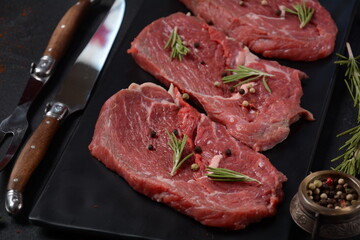 Three pieces of traditional thin steak cut from the tenderloin on wooden cutting board with olive oil, salt, rosemary and pepper. Raw Black Angus Prime meat steaks suitable for grilling on frying pan.