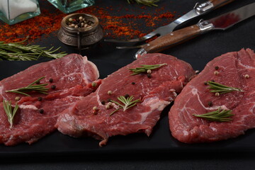 Three pieces of traditional thin steak cut from the tenderloin on wooden cutting board with olive oil, salt, rosemary and pepper. Raw Black Angus Prime meat steaks suitable for grilling on frying pan.