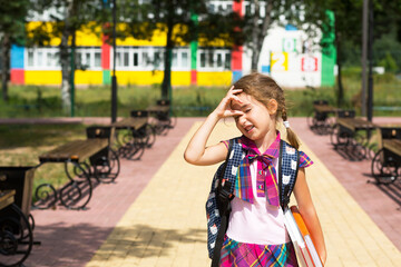 Fototapeta premium Girl with a backpack and a stack of books near the school. Back to school, the child is tired, heavy textbooks. Education, primary school classes, the beginning of the school year, September 1