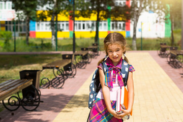 Obraz premium Girl with a backpack and a stack of books near the school. Back to school, the child is tired, heavy textbooks. Education, primary school classes, the beginning of the school year, September 1