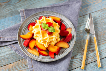 Traditional classic Belgian or Brussels waffles with red plums in a ceramic plate on a blue wooden culinary background closeup	
