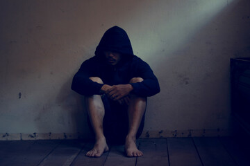 Depressed and hopeless asian man sitting alone after using drugs sitting on the floor. Drugs addiction and withdrawal symptoms concept.