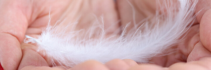 Woman holding soft white feather in her hands closeup