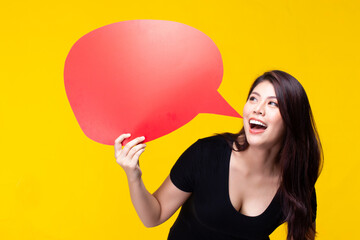 Attractive beautiful young asian woman smile and excited holding empty speech bubble isolated on yellow background.