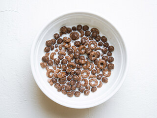 White ceramic plate with chocolate breakfast cereal and milk.