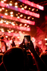 Music fan silhouette taking a photograph with a smartphone of a blurred musician at a concert with...