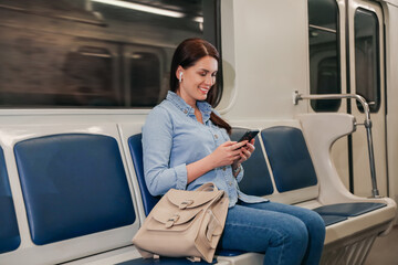 Beautiful woman with mobile phone and earbuds listening to music in subway train. Public transport
