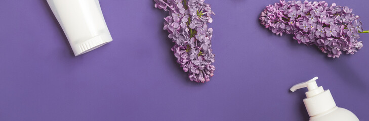 Set of hair care cosmetic products and lilac flowers on violet table bzckground, flat lay. banner