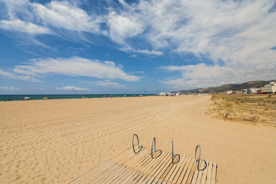 Castelldefels beach with sand dunes and stand for bicycles. Sunny day with blue sea and sky.