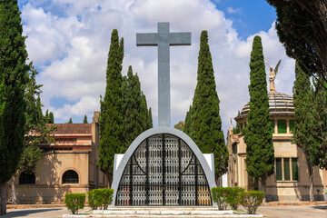 A view of the cemetery with a large cross in the center and pantheons and cypress trees