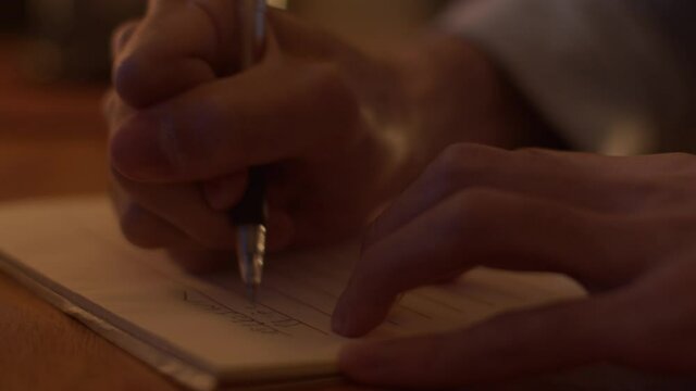 Man's hand in tight close-up as letter is being written in dimly lit room