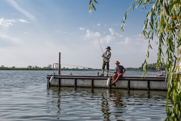 Fototapeta premium two men on the pier are fishing with fishing rods in the summer