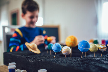 Happy school boy make a solar system for a school science project at home