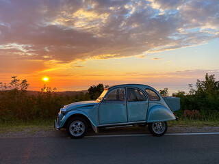 Fototapeta na wymiar Vintage blue car on the road in beautiful sunset light. Green hills at the Adriatic seaside