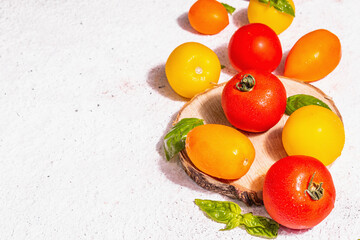 Assortment ripe tomatoes with fresh basil leaves on white putty background