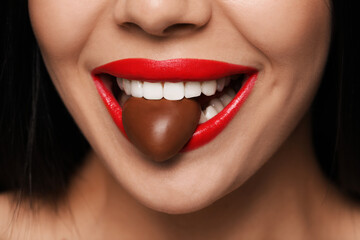 Obraz premium Young woman with red lips eating heart shaped chocolate candy, closeup