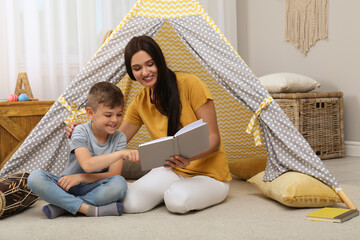Mother and son reading book near toy wigwam at home © New Africa