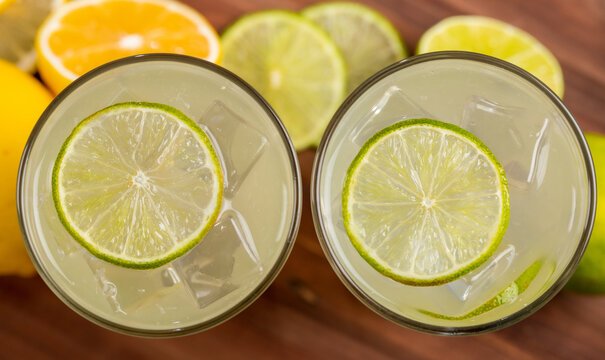 A close up picture of two refreshing glasses of cold fruit juice with straw, ice lime and lemon juice, decorating with fresh lime and lemon on wooden table. Concept for refreshing