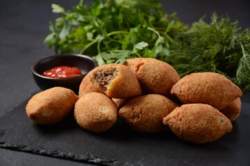 Deep fried kibbeh of ground beef meat mixed with bulgur, stuffed with fried minced meat with pine nuts on cutting board on dark background