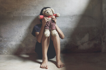 Child covered her face sitting alone on floor with her bear in dark room. concept for bullying, depression stress or frustration.