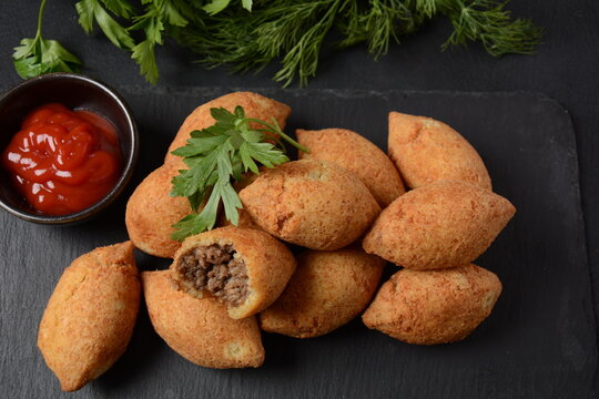 Deep fried kibbeh of ground beef meat mixed with bulgur, stuffed with fried minced meat with pine nuts on cutting board on dark background