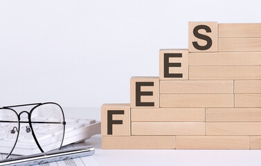 Wooden cubes with letters FEES on the white table with keyboard and glasses
