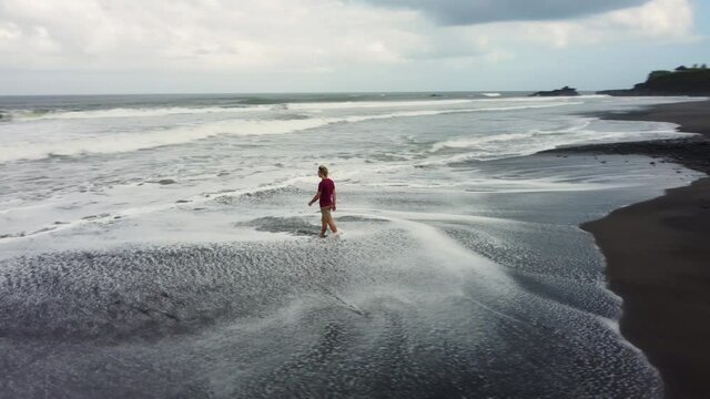 Man walking on black sand Bailan beach in Bali before storm. High quality 4k aerial footage
