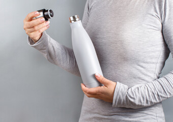 Woman in grey tee holding grey insulated bottle on grey background