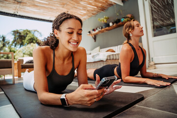 Two friends cooling down after exercising one stretching one typing on cellular device
