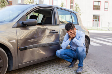 Portrait of man wearing jeans and blue shirt broken his car, being upset and covering his face with...