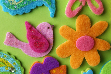 Different small colorful felt items on green background, flat lay