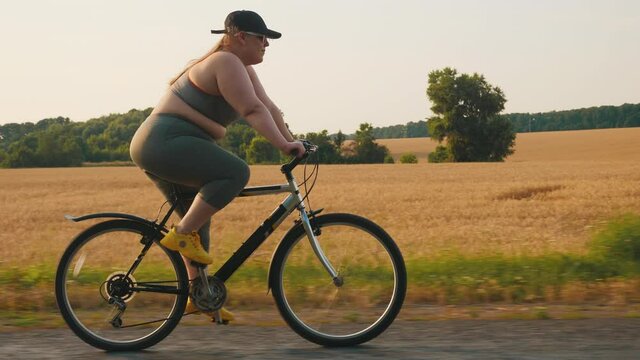 Young plus size woman rides a sports bike on the road outside the city. Overweight woman exercising to lose weight